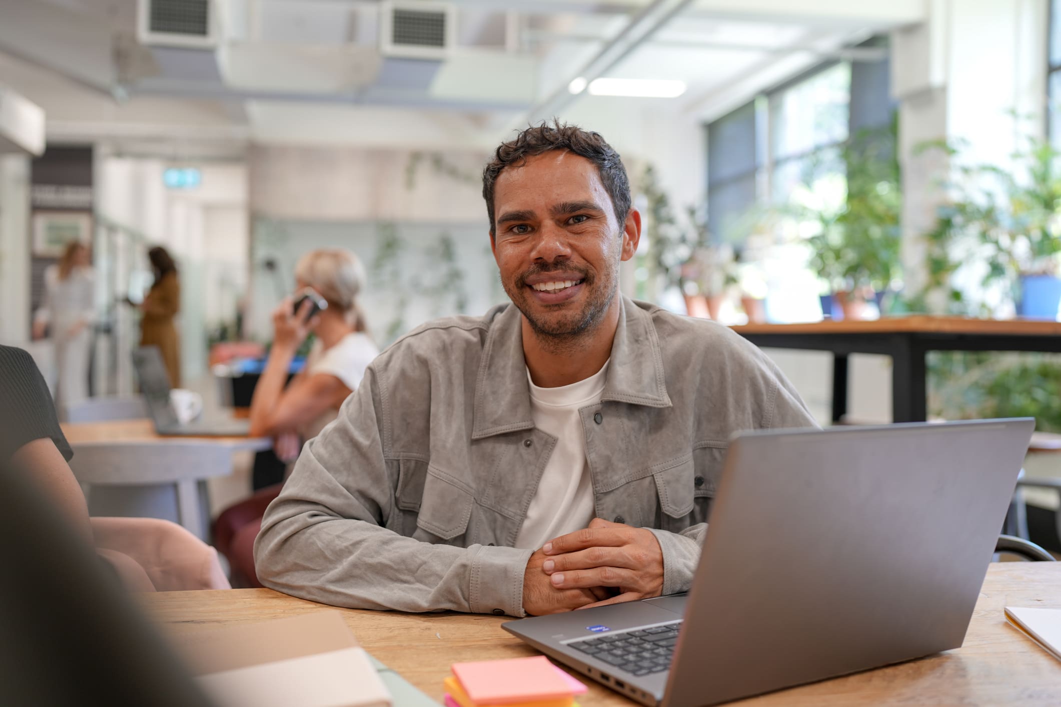 Man smiling while working on a laptop in a bright office.