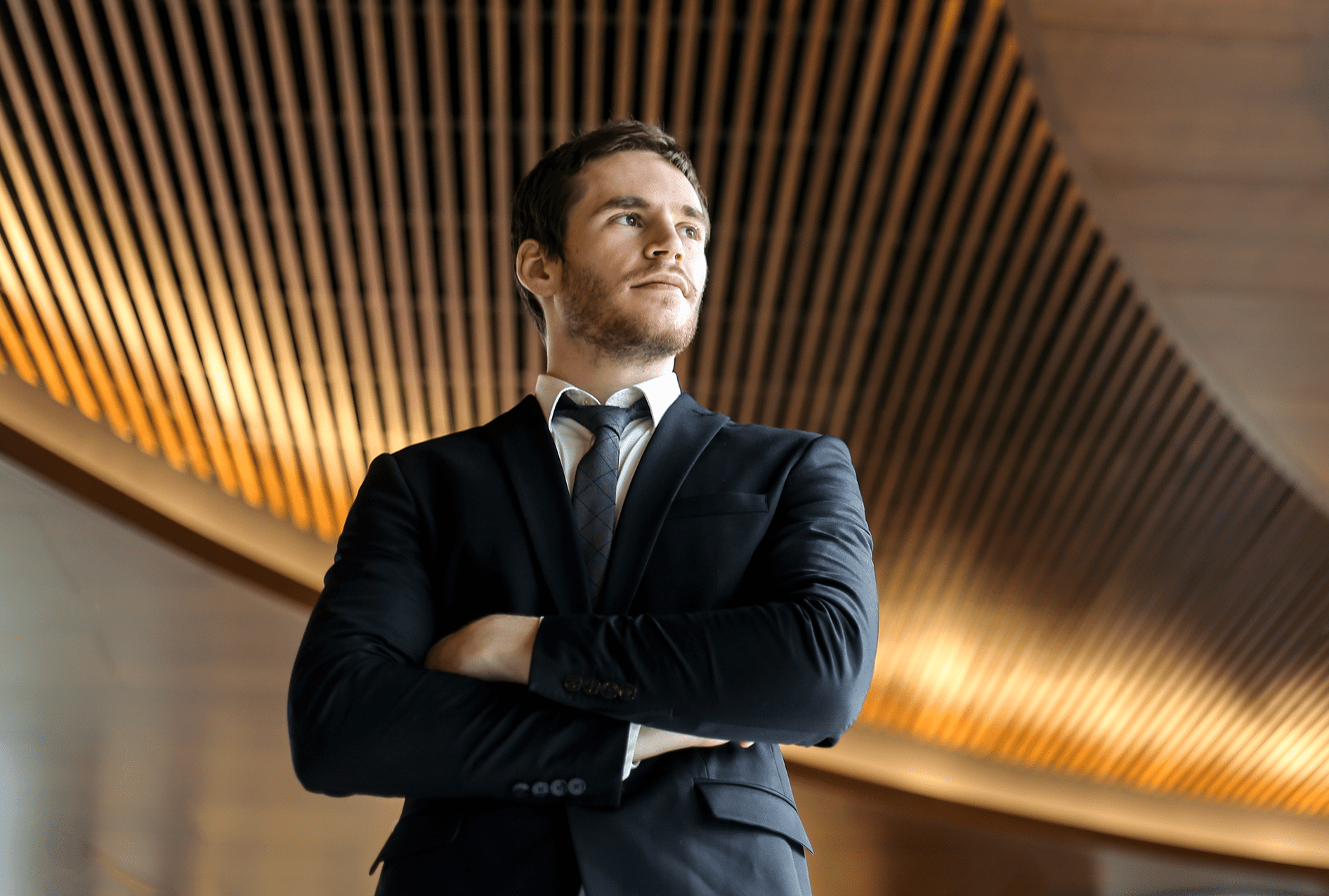 Confident businessman standing with arms crossed under modern wooden ceiling.