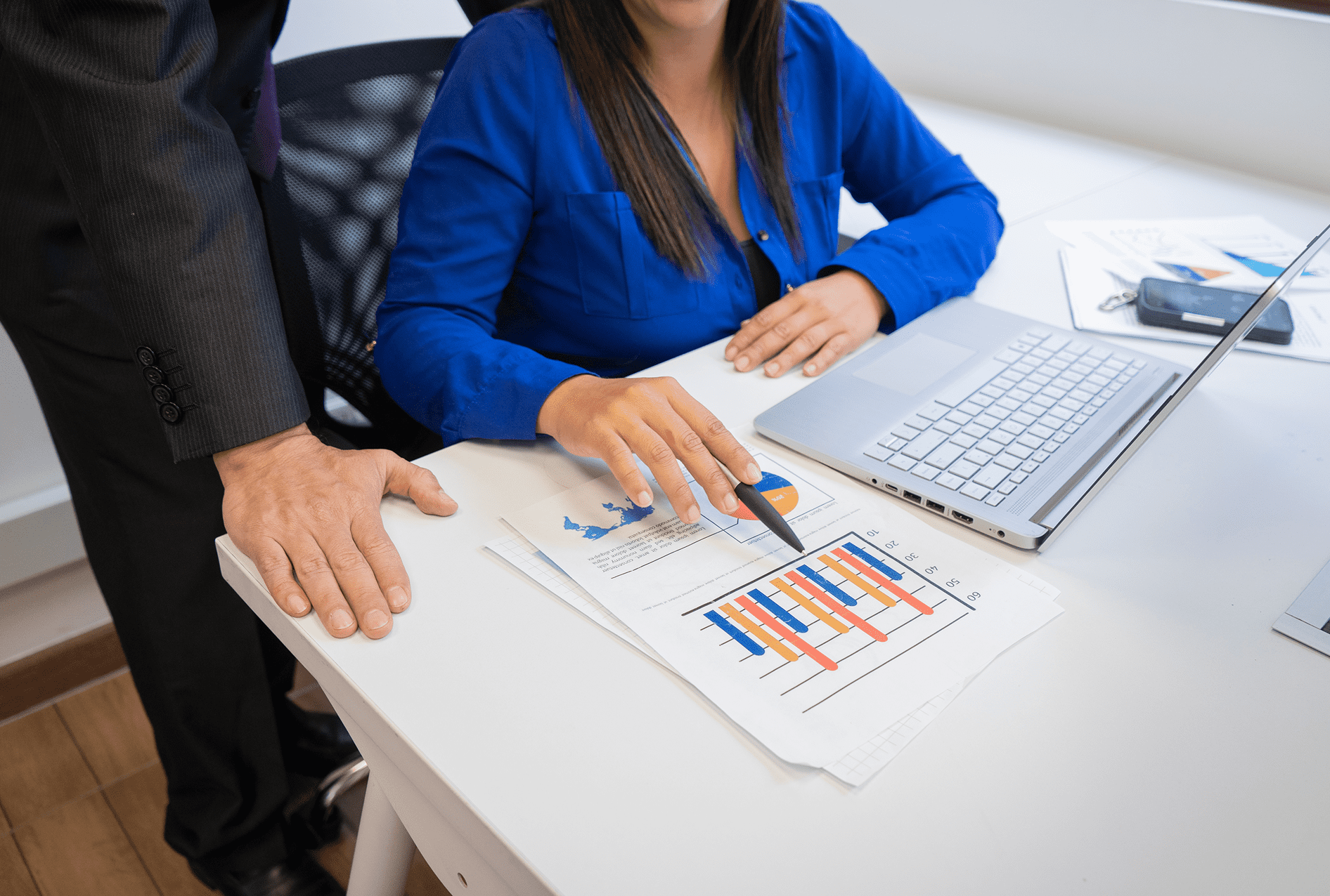 Two professionals discussing a business chart at a desk with a laptop.