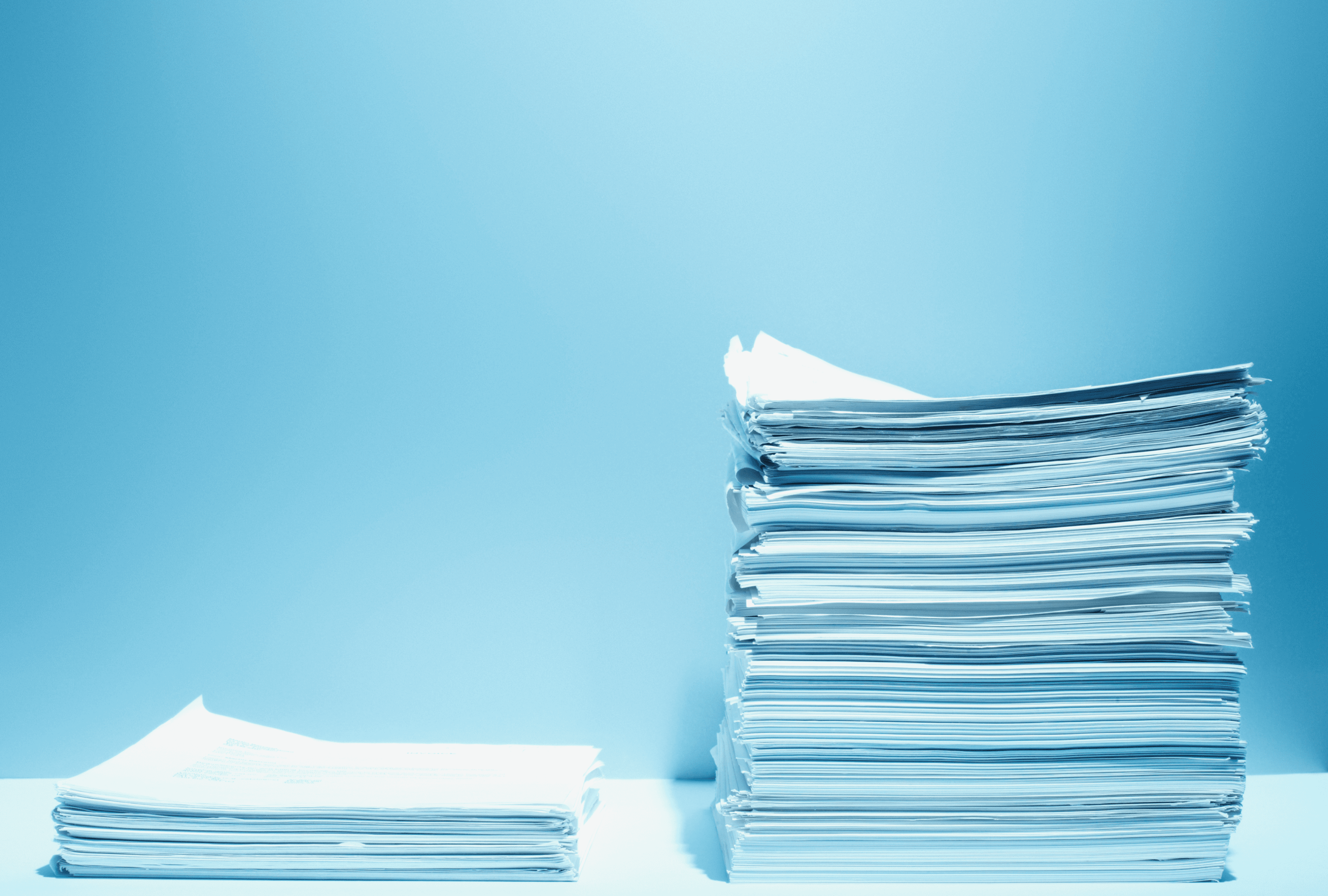 A tall stack of papers beside a smaller pile against a blue background.