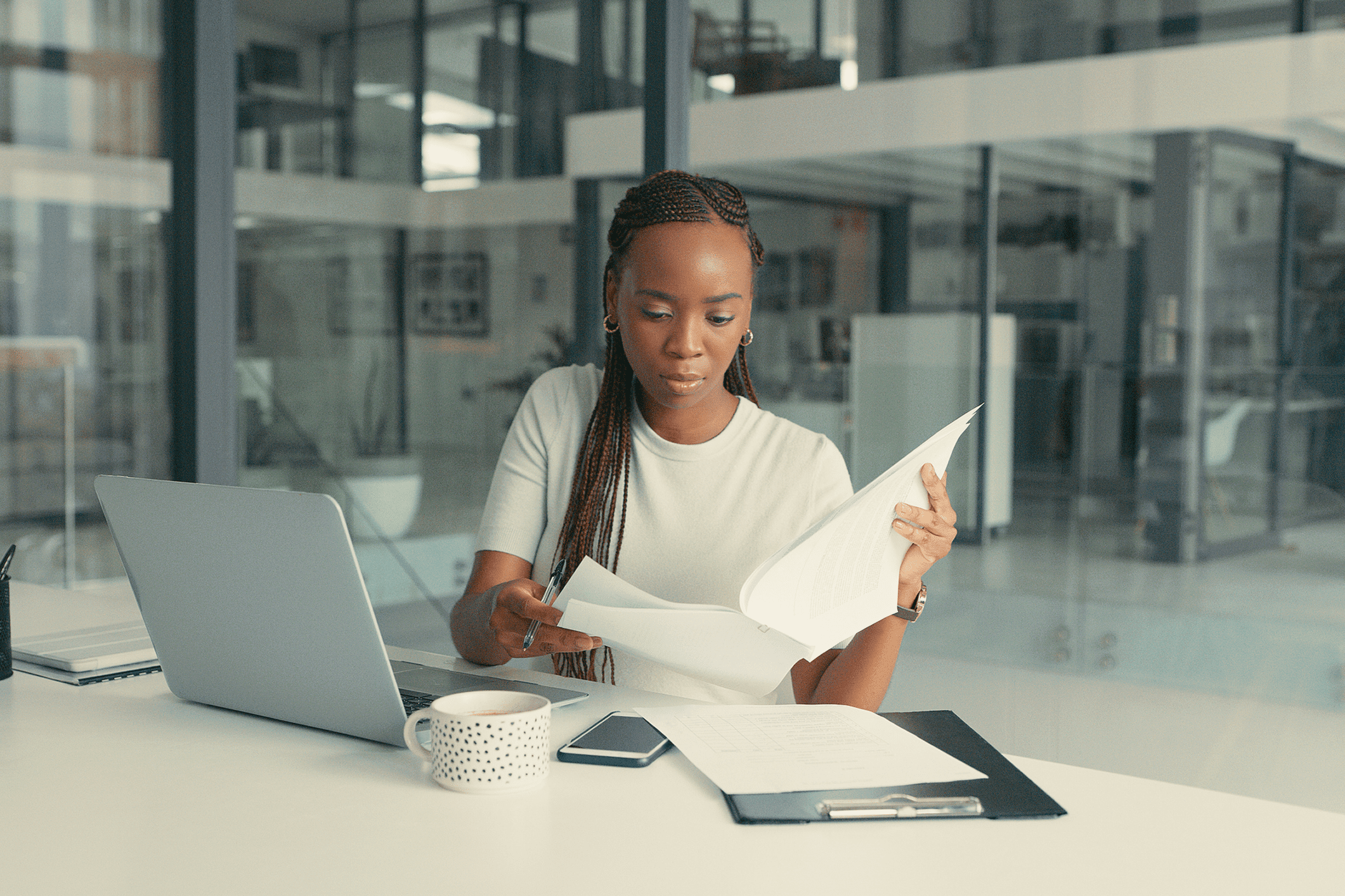 Focused woman reviewing documents at a desk with a laptop and coffee.