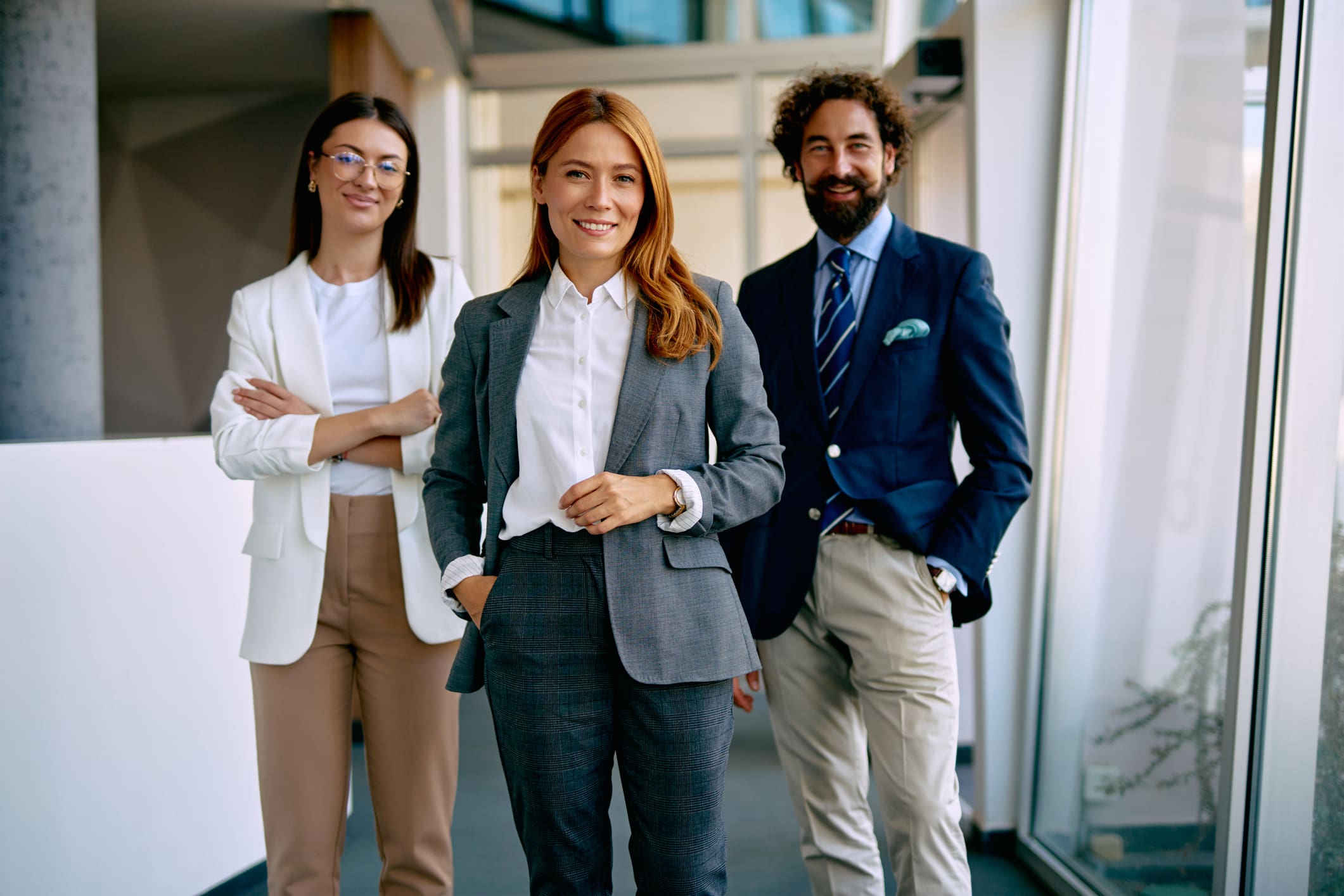 Three confident professionals posing in an office hallway.