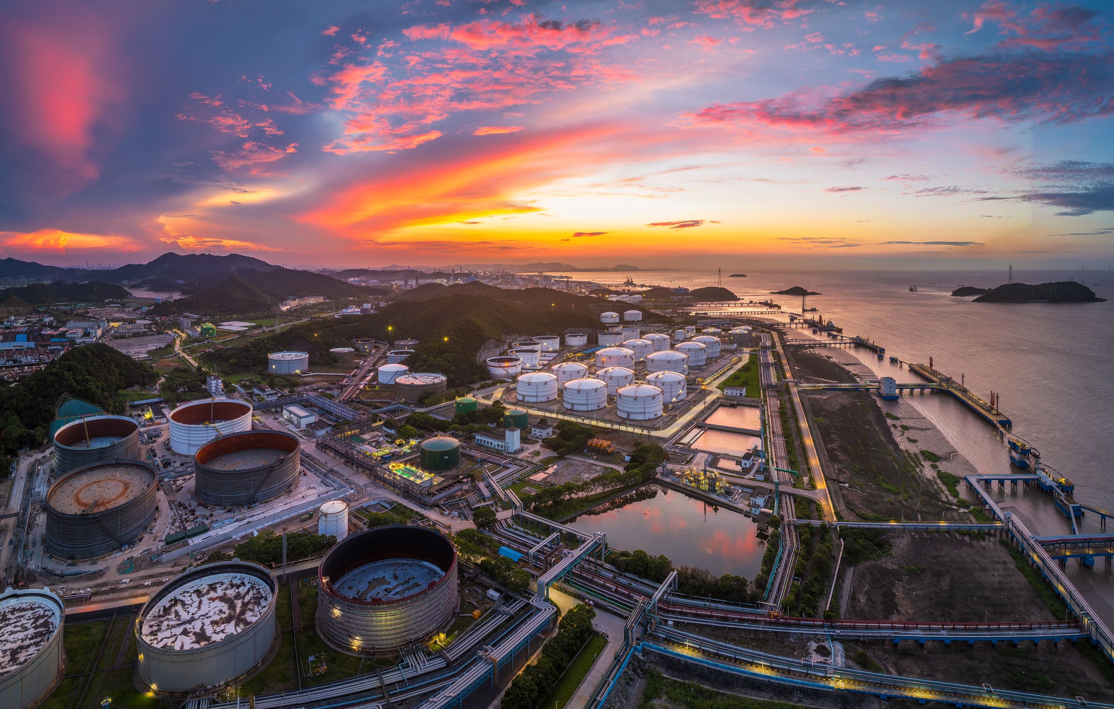 Sunset over an industrial coastal area with colorful skies.